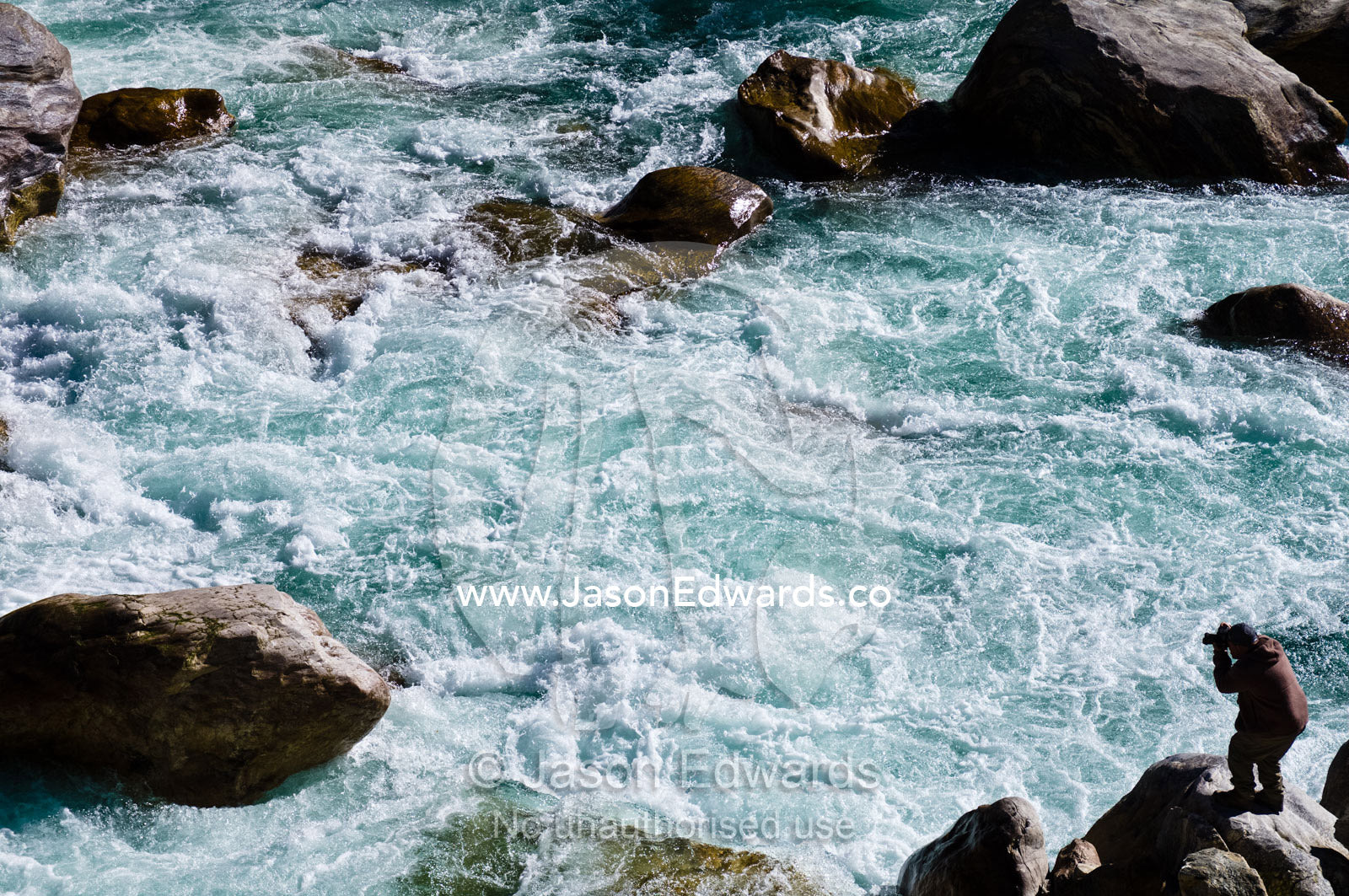 A photographer captures the swirling rapids of a pristine Himalaya river from a boulder on the shore. Punakha River, Punakha Valley, Punakha-Wangdiphodrang District, Bhutan.