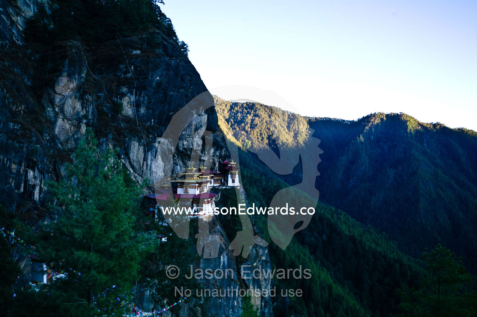 An ancient Buddhist monastery perched on a sheer cliff face above a forested valley in the Himalaya. Paro Taktsang, The Tigers Nest, Paro Valley, Paro District, Bhutan.