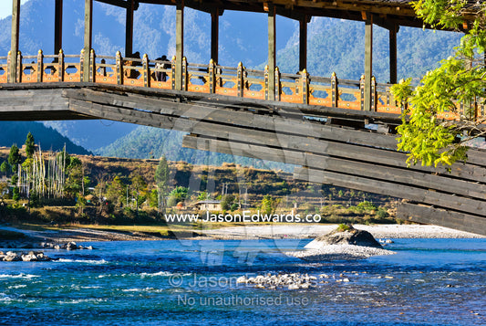 An antique timber footbridge arches over the aqua waters of a Himalayan river. Punakha Dzong, Punakha dzongkhag, Punakha District, Bhutan.