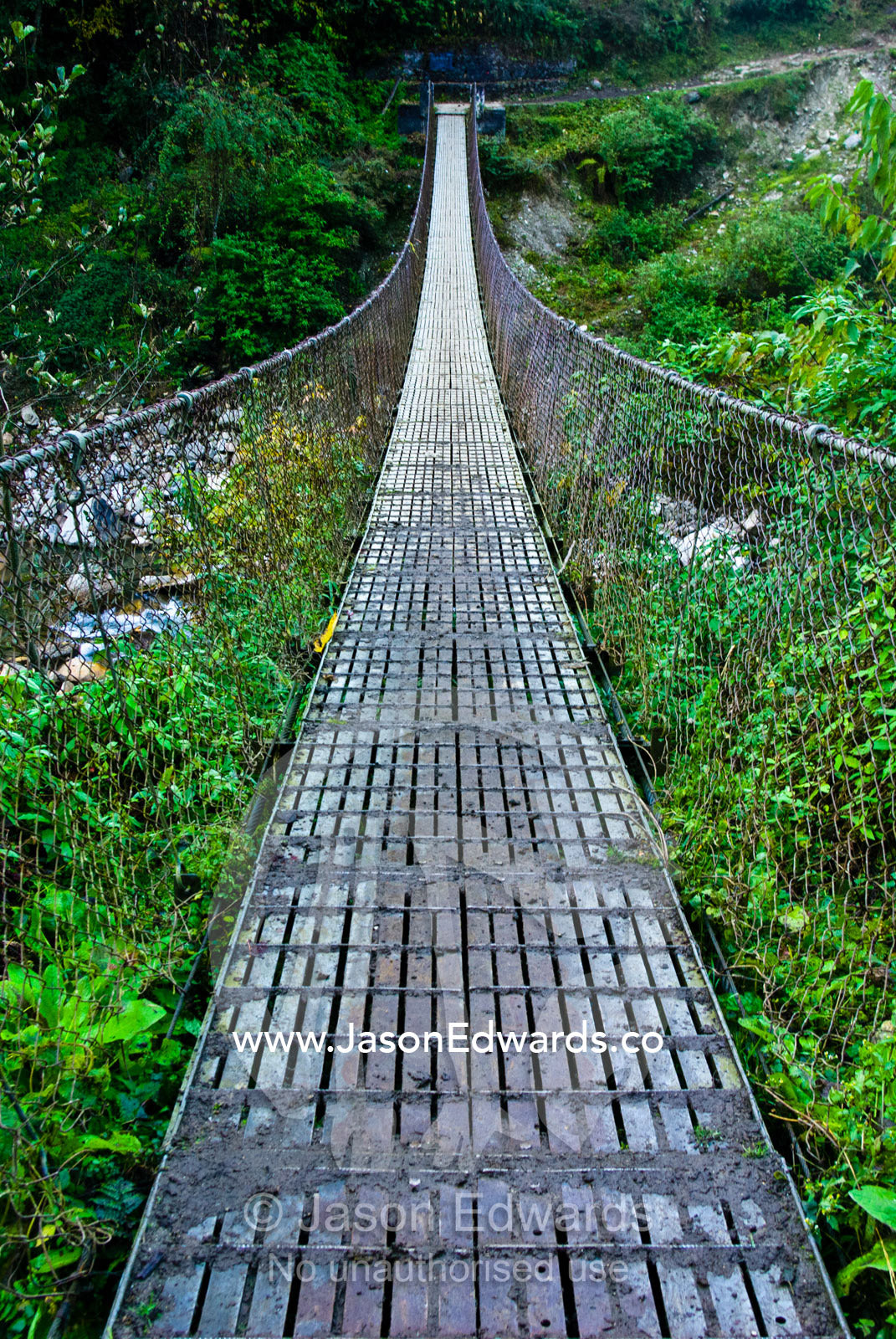 The metal planks of a suspension bridge cross between mountain valley walls in the Himalaya. Pho Chu, Pho River, Gasa Dzong, Gasa Tashi Tongmon Dzong, Gasa Gasa Dzongkhag District, Bhutan.