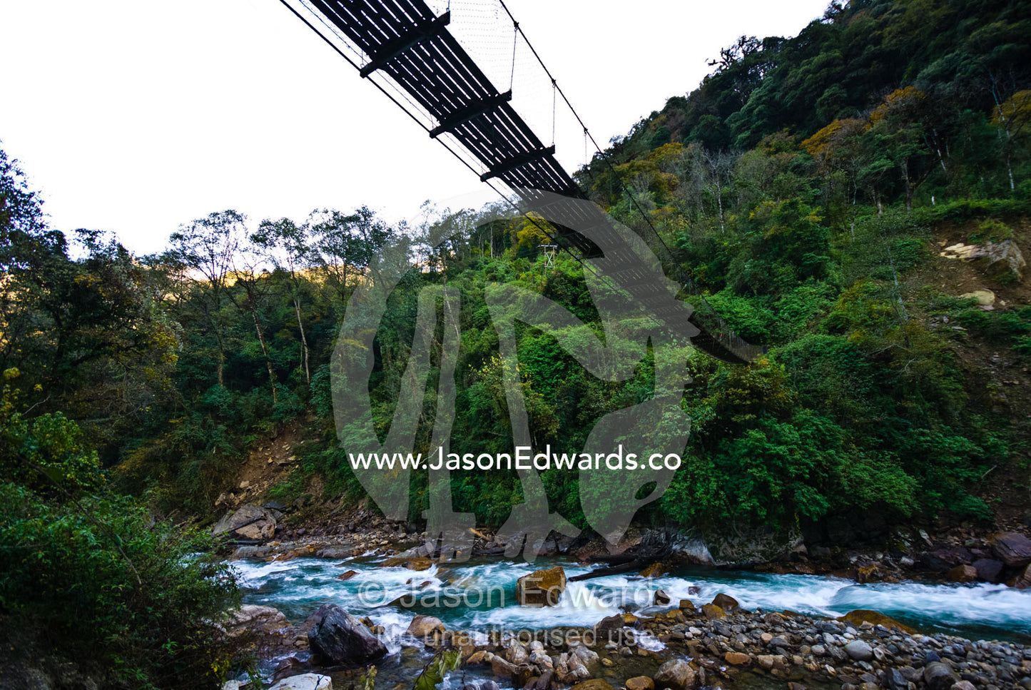The metal planks of a suspension bridge cross between mountain valley walls in the Himalaya. Pho Chu, Pho River, Gasa Dzong, Gasa Tashi Tongmon Dzong, Gasa Gasa Dzongkhag District, Bhutan.