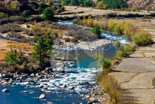 An alpine river cascades through a rocky riverbed past agriculture fields. Paro Chu, Paro River, Paro, Paro District, Bhutan.