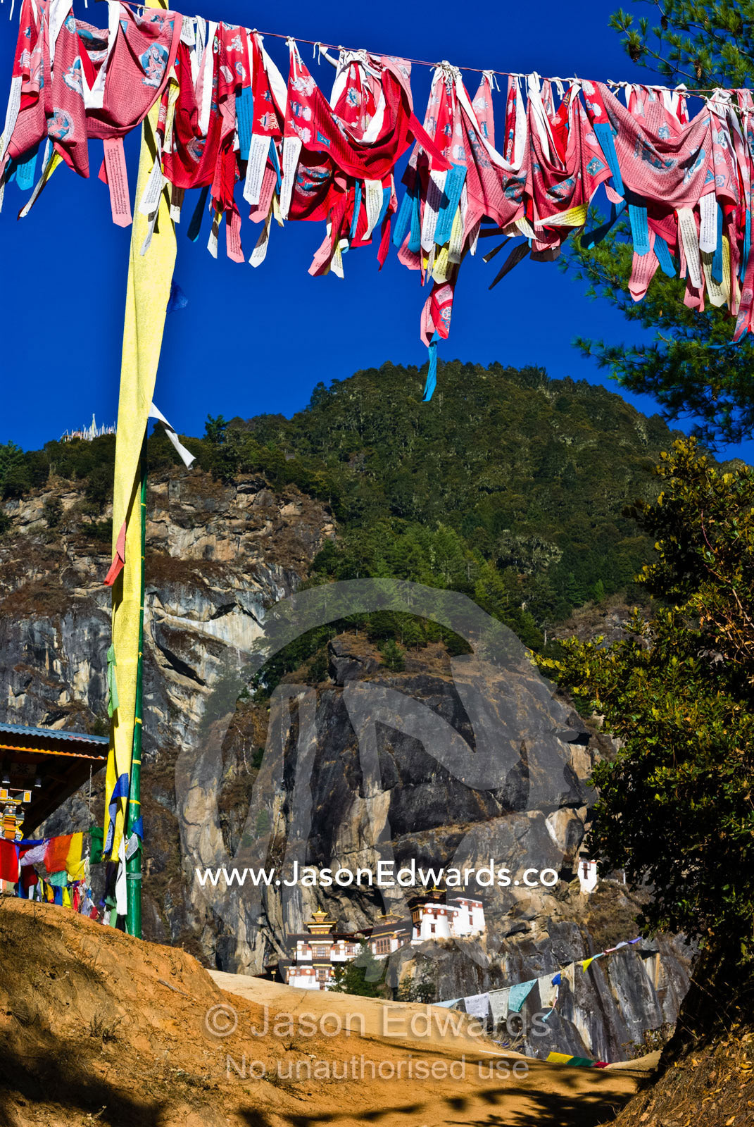 Bright red prayer flags flapping in the breeze on a Himalaya mountainside near a Buddhist monastery. Paro Taktsang, The Tigers Nest, Paro Valley, Paro District, Bhutan.