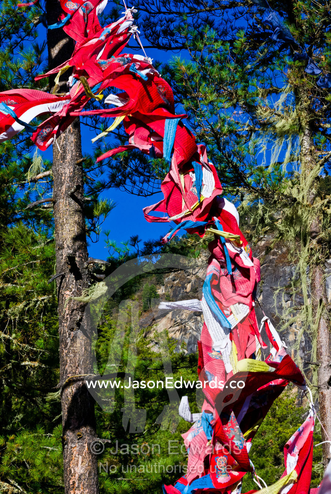 Bright red prayer flags flapping in the breeze on a Himalaya mountainside. Paro Taktsang, The Tigers Nest, Paro Valley, Paro District, Bhutan.