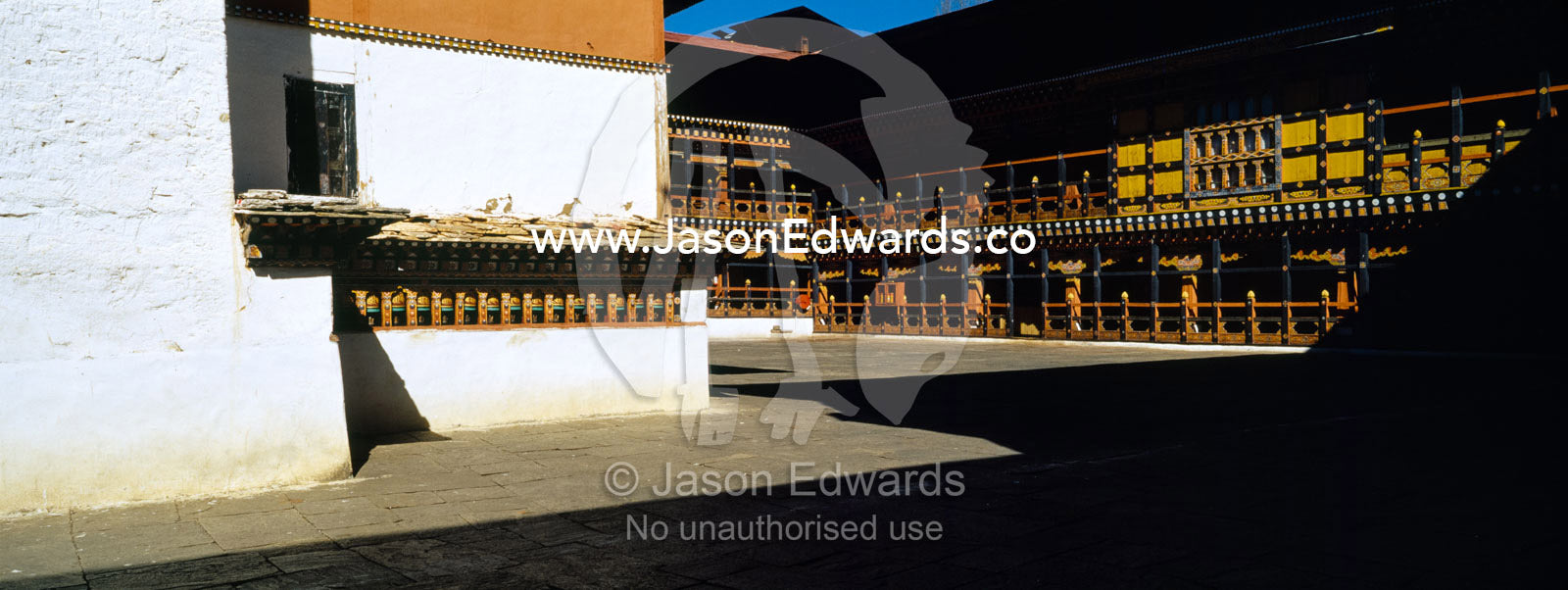 An ancient carved timber balcony and balustrade above a walkway in a Buddhist monastery courtyard. Rinpung Dzong, Paro Dzong, Paro, Paro District, Bhutan.