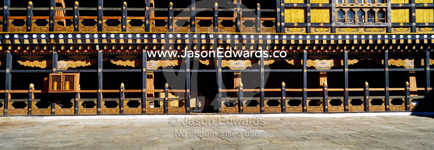 An ancient carved timber balcony and balustrade above a walkway in a Buddhist monastery courtyard. Rinpung Dzong, Paro Dzong, Paro, Paro District, Bhutan.
