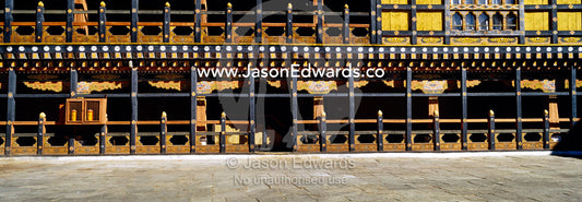 An ancient carved timber balcony and balustrade above a walkway in a Buddhist monastery courtyard. Rinpung Dzong, Paro Dzong, Paro, Paro District, Bhutan.