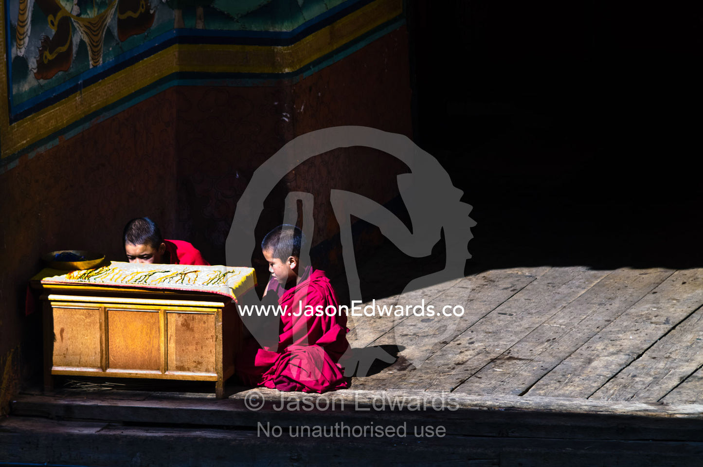 A pair of young Buddhist monks secretly look at music on their music device instead of weaving colored strips of wool. Rinpung Dzong, Paro Dzong, Paro, Paro District, Bhutan.