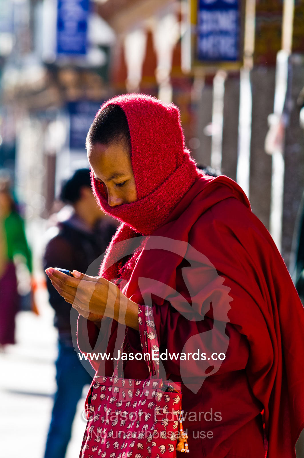 A Buddhist monk in red robes texting on a cell phone in the business district of a Himalayan town. Thimphu, Thimphu District, Bhutan.