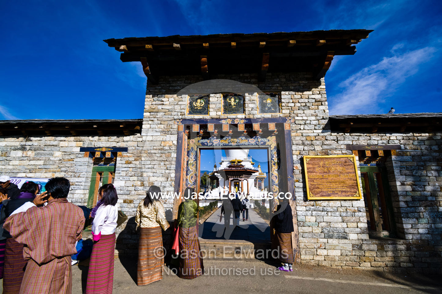 A Buddhist pilgrim talks on a cell phone whilst waiting at the entrance gate to offer prayers at the Memorial Chorten. Thimphu Memorial Chorten, Thimphu Bhutan.