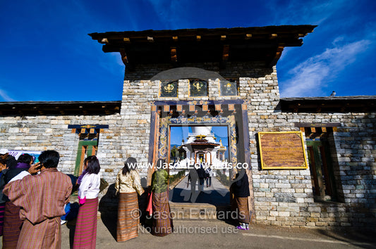 A Buddhist pilgrim talks on a cell phone whilst waiting at the entrance gate to offer prayers at the Memorial Chorten. Thimphu Memorial Chorten, Thimphu Bhutan.