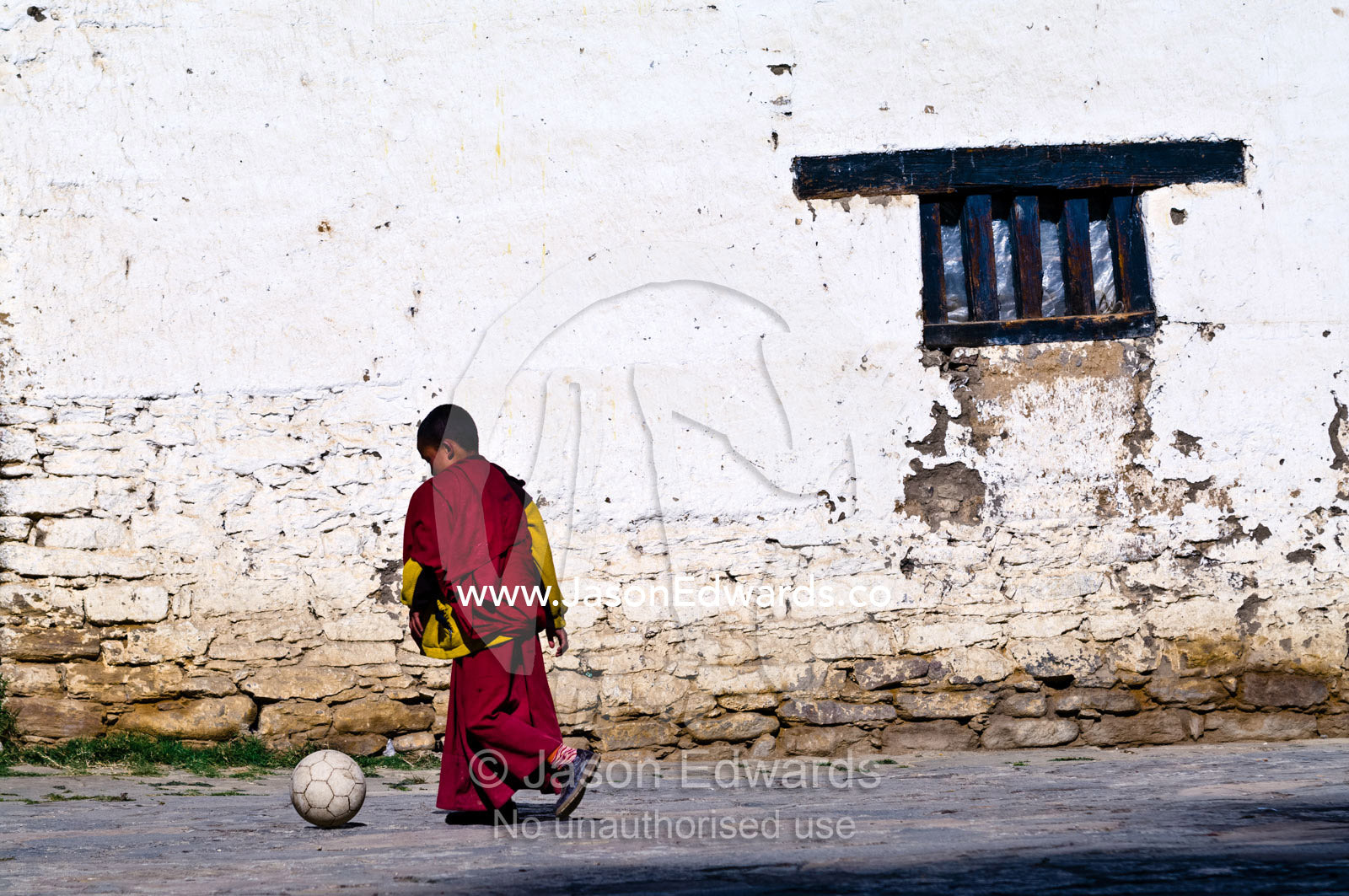 A young Buddhist monk kicks a football around the ancient courtyard of a Buddhist Astrology school. Pangri Zampa Astrology School, Thimphu, Thimphu District, Bhutan.