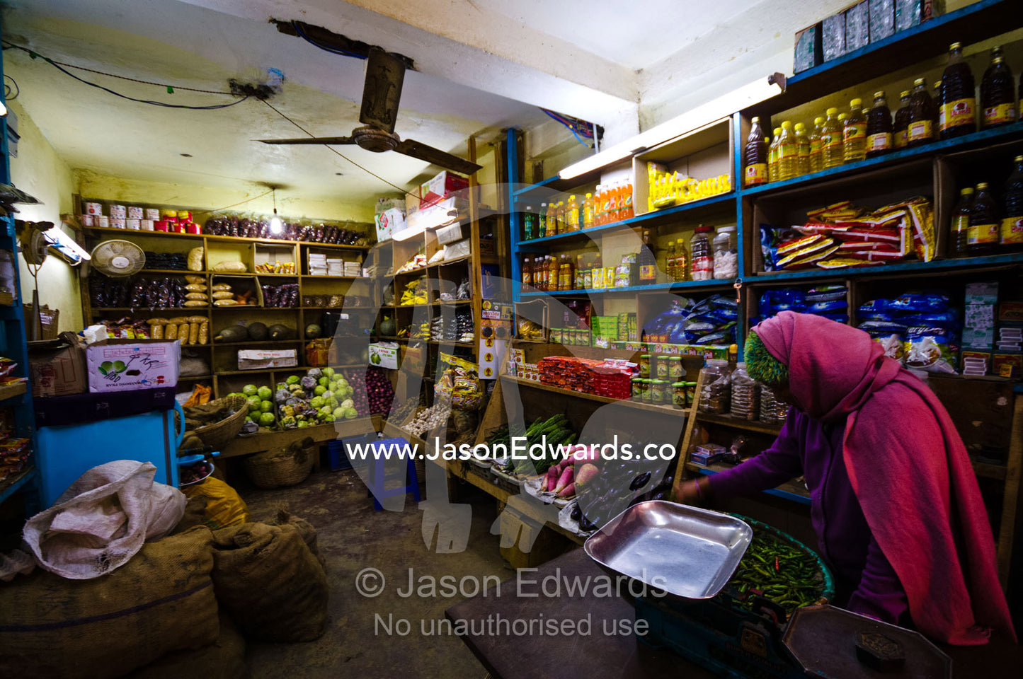 A shopkeeper prepares to weigh a tray of chile peppers in a greengrocer general store. Thimphu, Thimphu District, Bhutan.