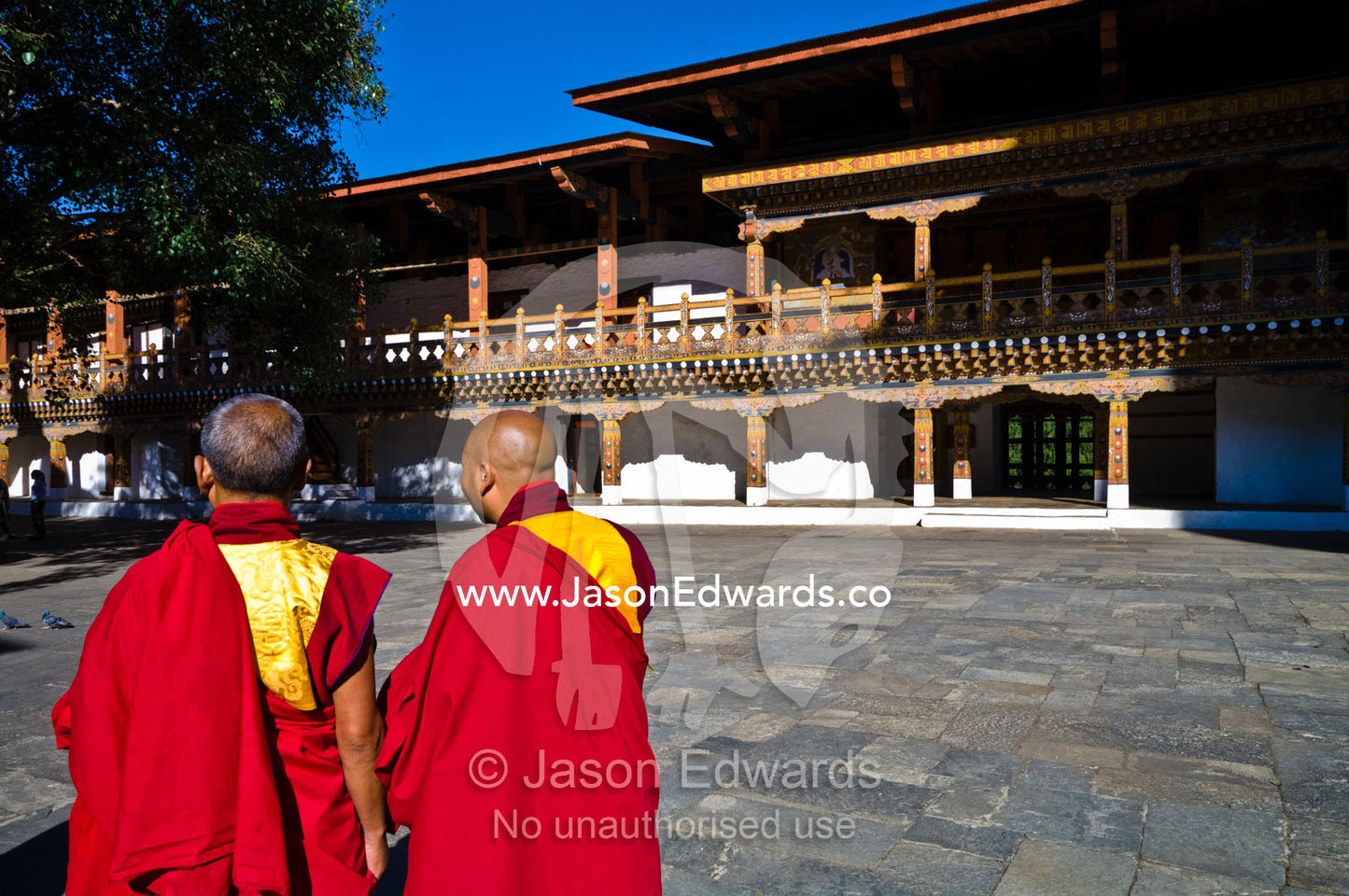 Buddhist monks in red and gold robes deep in conversation in the paved courtyard of an ancient monastery. Punakha Dzong, Punakha dzongkhag, Punakha District, Bhutan.