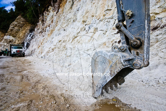 The huge bucket and blade of a road construction excavator scouring away at a cliff face in the Himalaya. Punakha District, Bhutan.