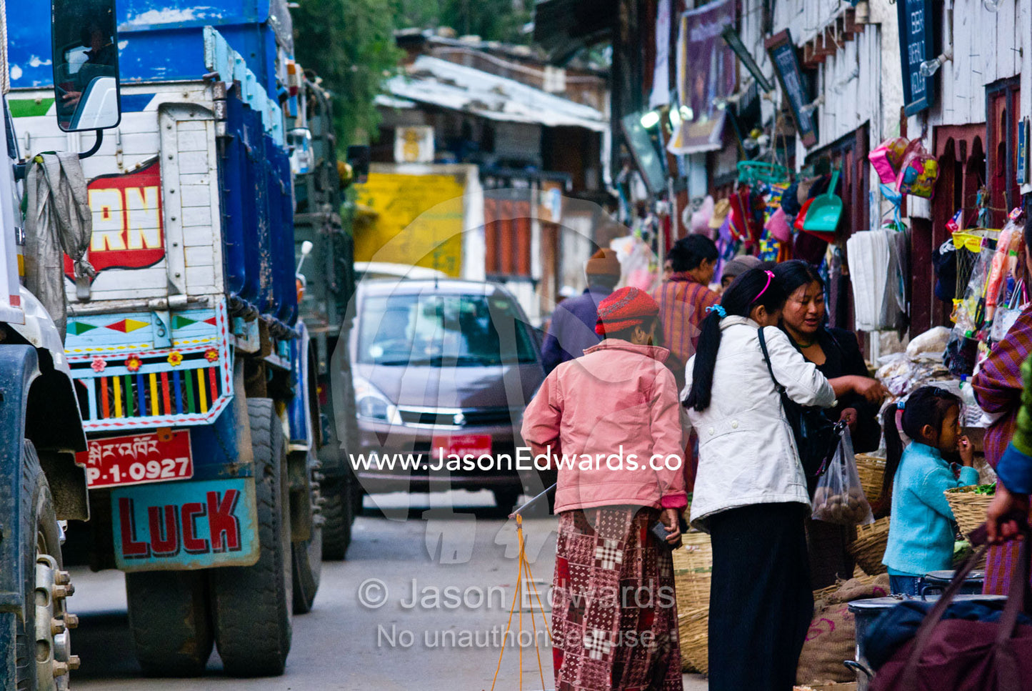 Women shopping in a roadside store whilst construction trucks and traffic congestion fill the main street. Wangdi, Wangdue Phodrang, Wangdue Phodrang District, Bhutan.