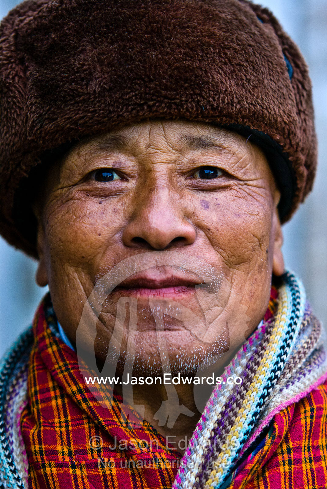A seventy-four year old retired government minister staying warm in his fur-lined hat and colorful scarf. Wangdi, Wangdue Phodrang, Wangdue Phodrang District, Bhutan.