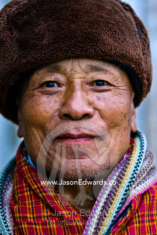A seventy-four year old retired government minister staying warm in his fur-lined hat and colorful scarf. Wangdi, Wangdue Phodrang, Wangdue Phodrang District, Bhutan.
