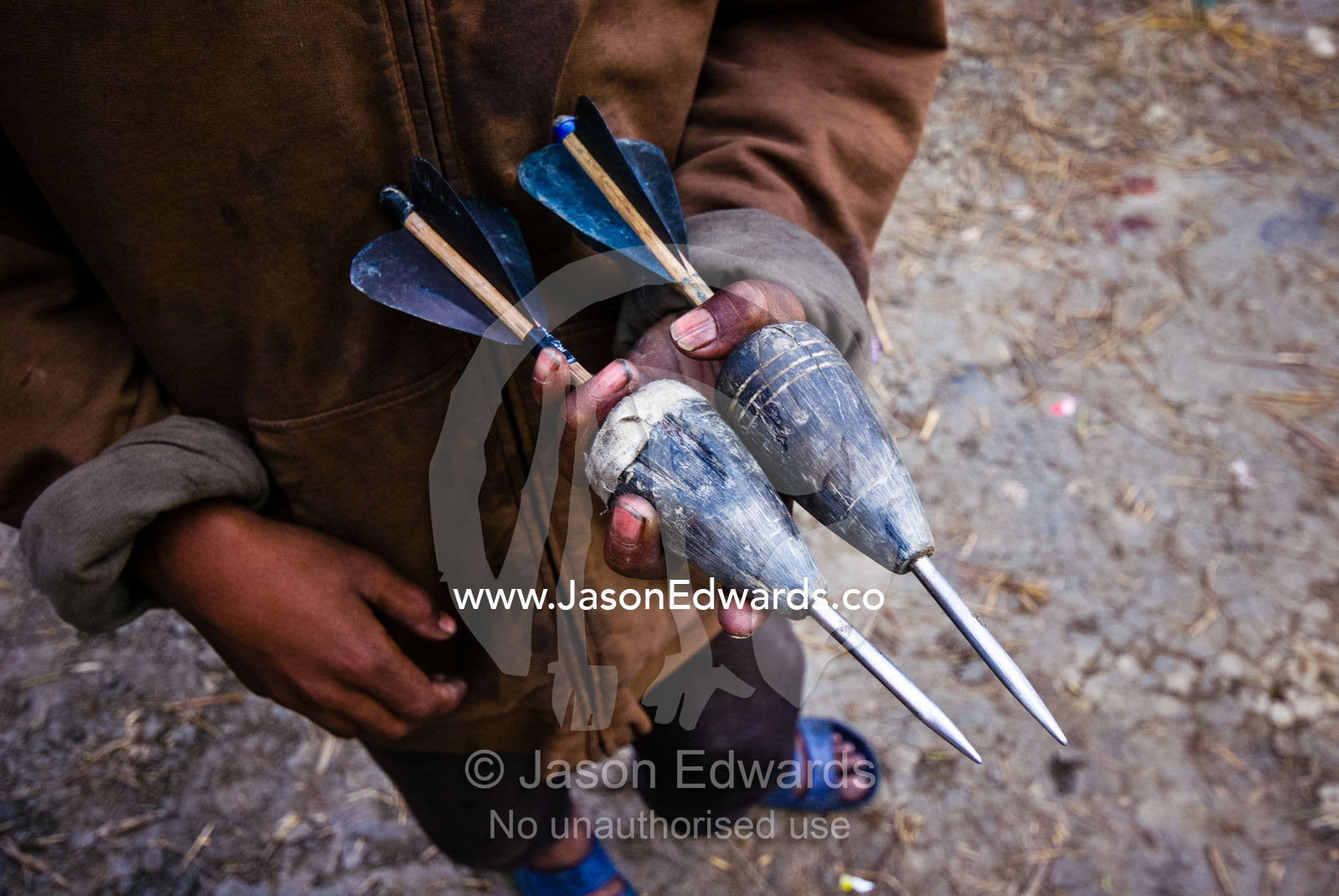 A village boy holding two large wooden darts known as khuru played during festivals. Punakha River, Punakha Valley, Punakha-Wangdiphodrang District, Bhutan.