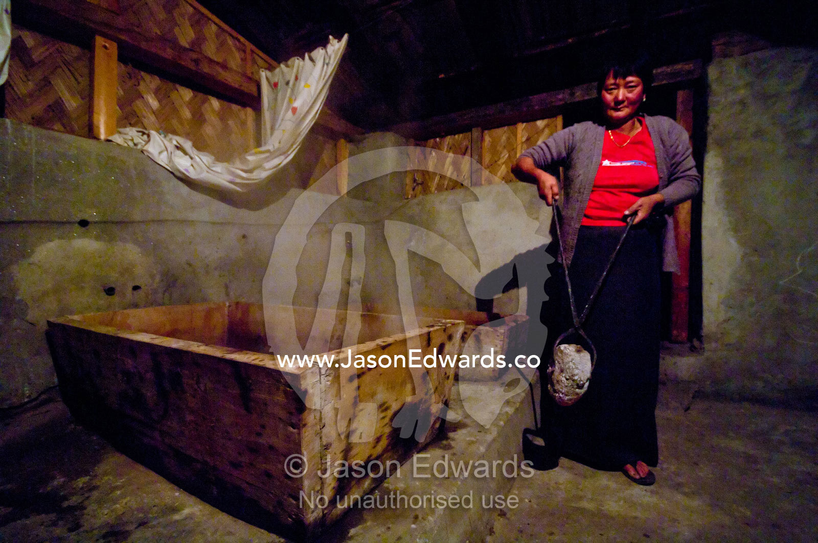 A farmers wife loads a hot rock into a timber bath to heat the icy river water for bathing. Thimphu, Thimphu District, Bhutan.