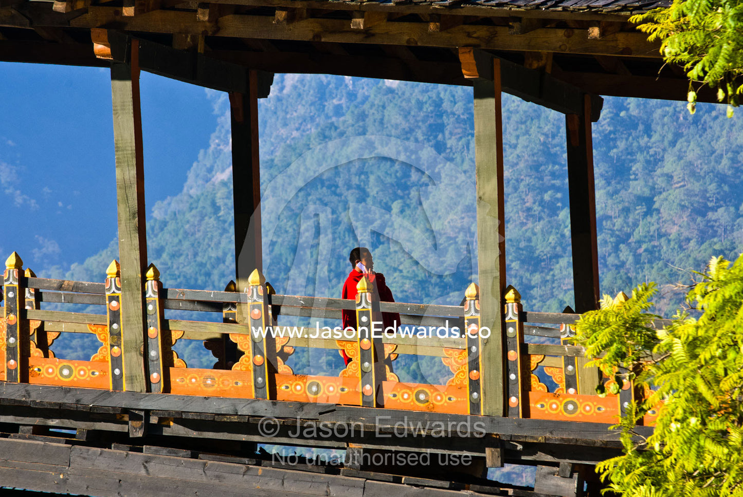 A Buddhist monk crosses an ancient timber bridge to a monastery talking on his cell phone. Punakha Dzong, Punakha dzongkhag, Punakha District, Bhutan.