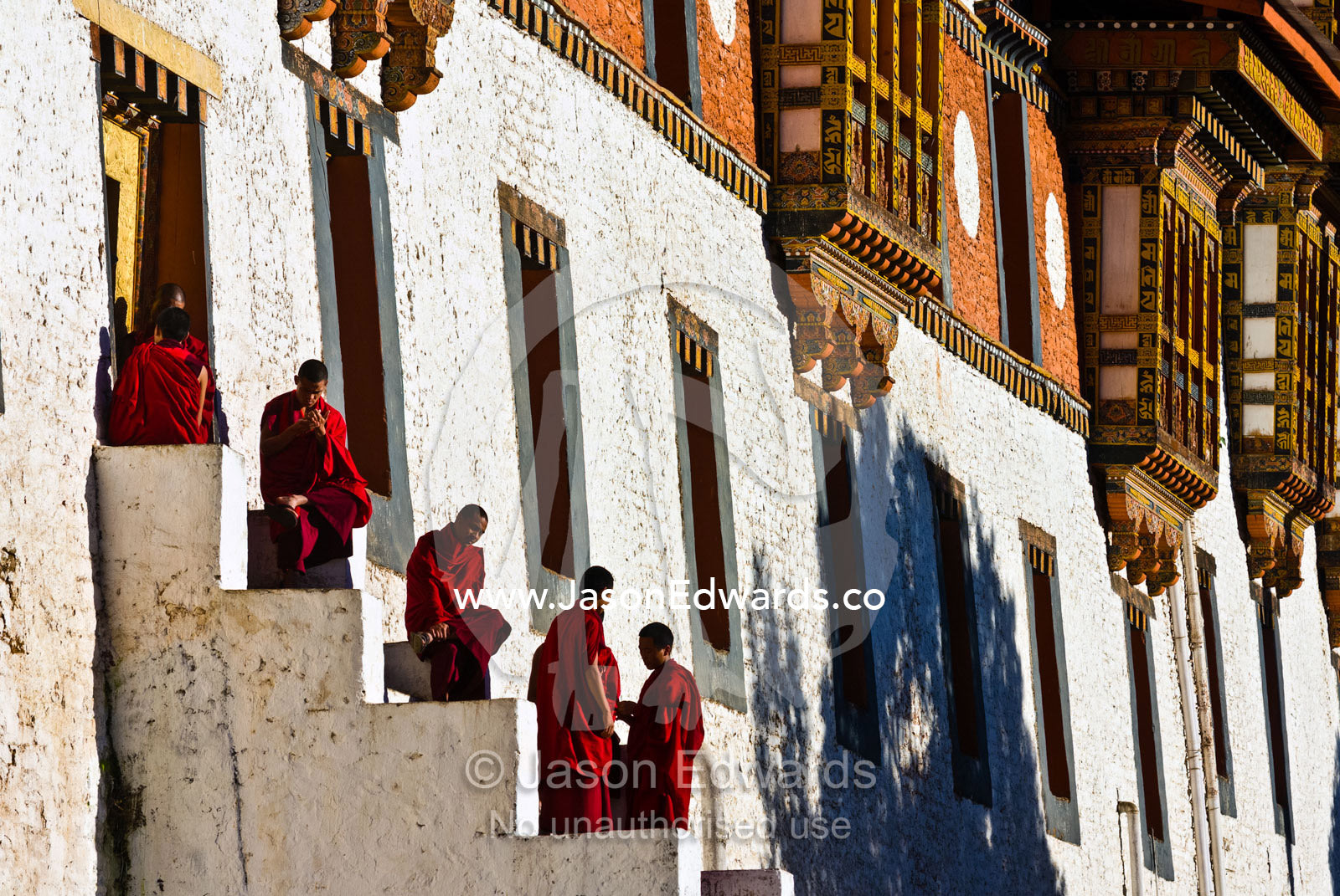 Buddhist monks gather on the steps on an ancient monastery in the afternoon sunlight to relax and enjoy conversation. Punakha Dzong, Punakha Dzongkhag, Punakha District, Bhutan.