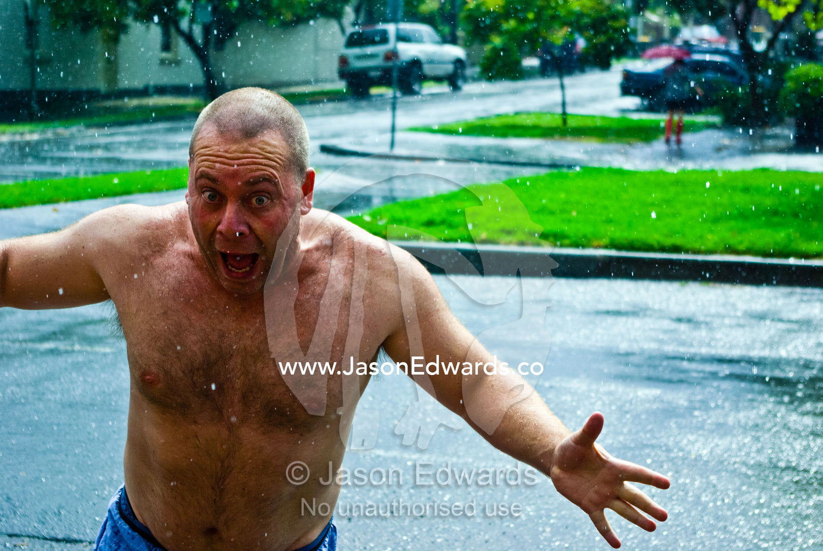 A man runs around in a summer rain storm downpour on Christmas Day. Carlton North, Melbourne, Victoria, Australia.
