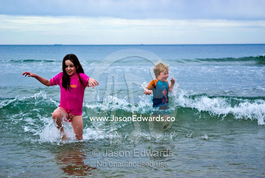 Children play in the waves on a cold winters day at the beach. Torquay, Surf Coast, Victoria, Australia.