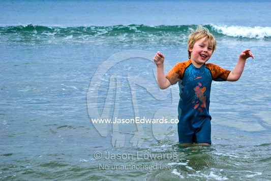 A boy plays in the waves on a cold winters day at the beach. Torquay, Surf Coast, Victoria, Australia.