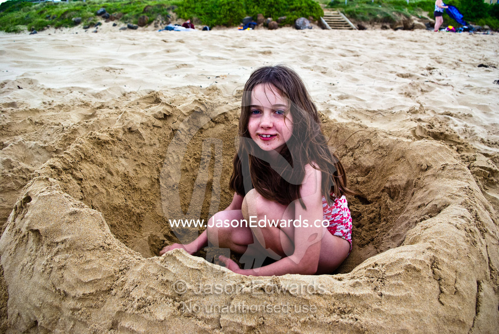 A girl digs a deep hole on a beach and makes a wall of sand around it. Torquay, Surf Coast, Victoria, Australia.