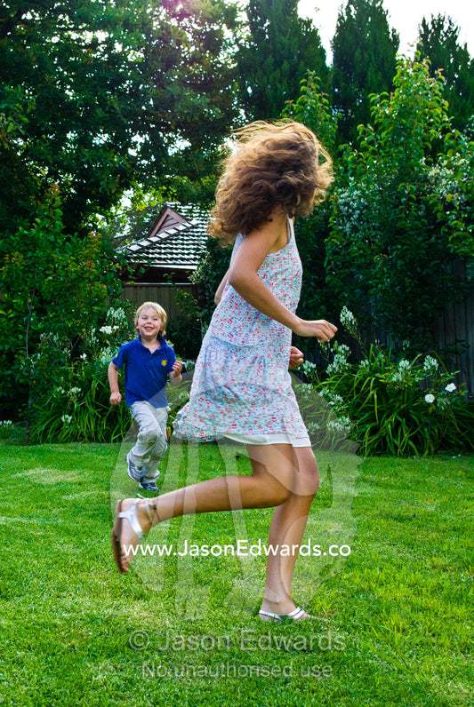 A young boy chases a teenage girl running and playing in a backyard. Malvern East, Melbourne, Victoria, Australia.