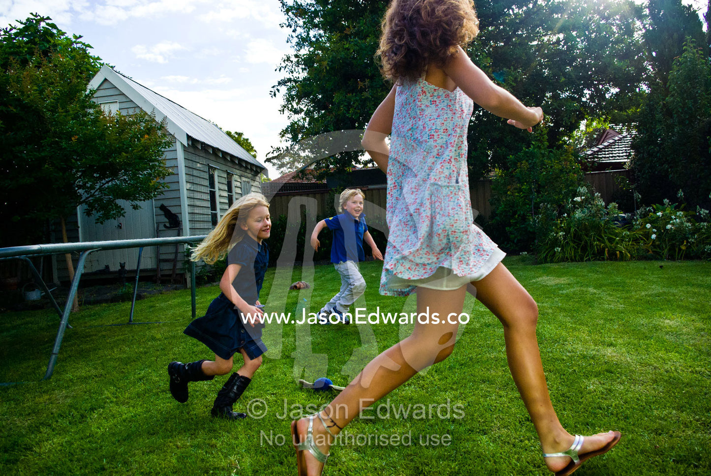 Young children chase a teenage girl running and playing in a backyard. Malvern East, Melbourne, Victoria, Australia.
