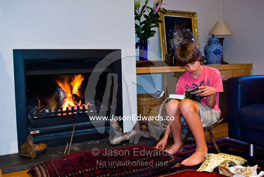 A teenage boy reads a novel he received for christmas by an open fire. Malvern East, Melbourne, Victoria, Australia.