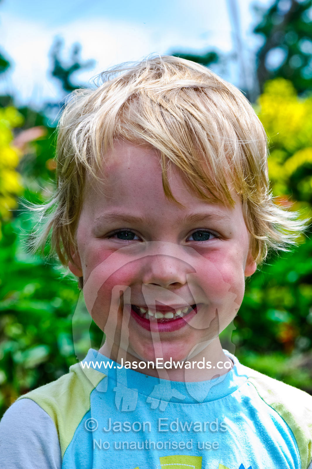 A smiling and happy blonde-haired boy in a garden on a summers day. Taveuni Island, Pacific Ocean, Fiji Islands.