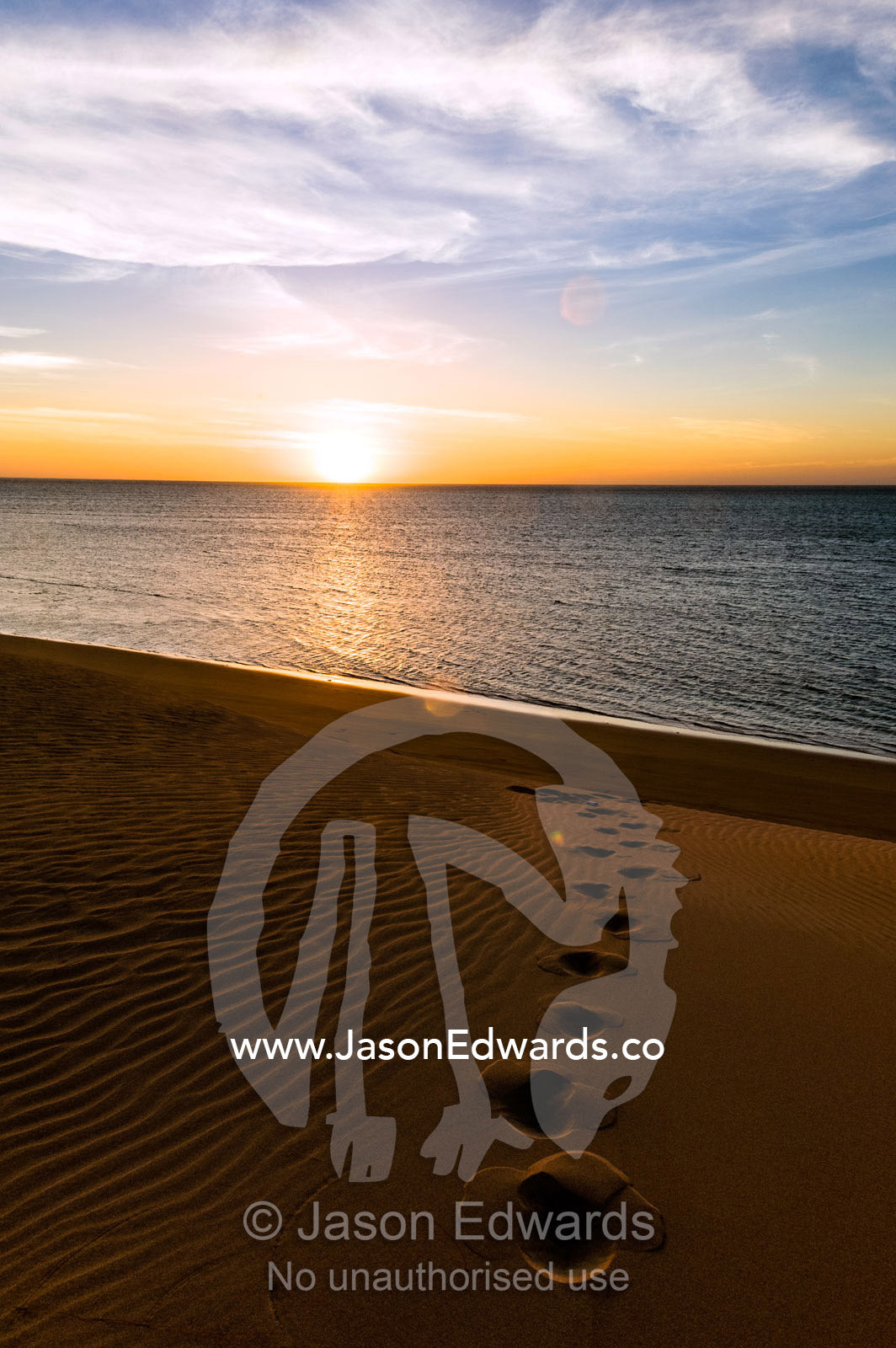 Footprints lead down a sand dune at sunset to a deserted ocean beach. Cape Range National Park, Exmouth, Ningaloo Reef, Western Australia, Australia.