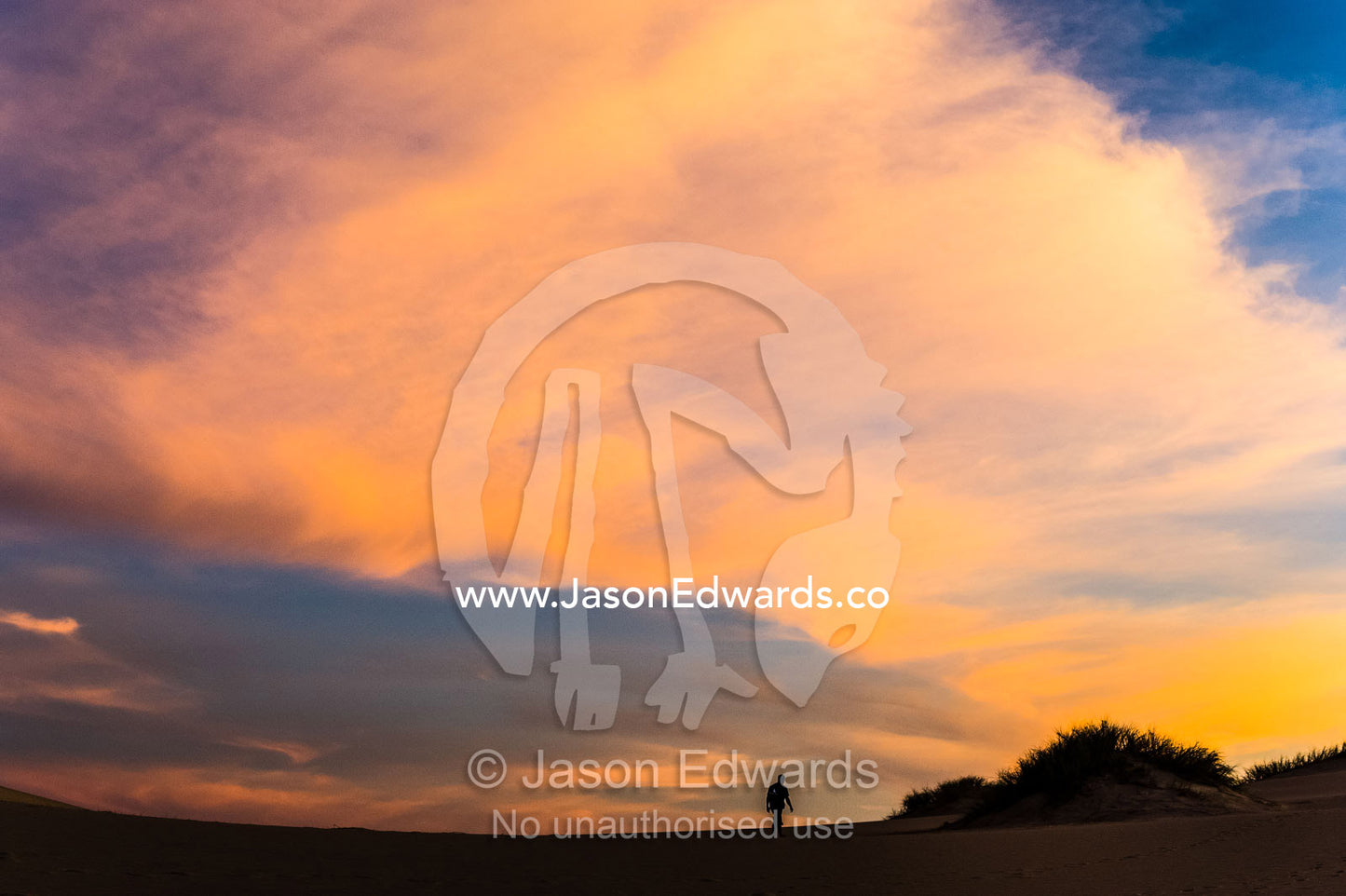 A lone hiker crosses a sand dune beneath pastel sunset clouds. Cape Range National Park, Exmouth, Ningaloo Reef, Western Australia, Australia.