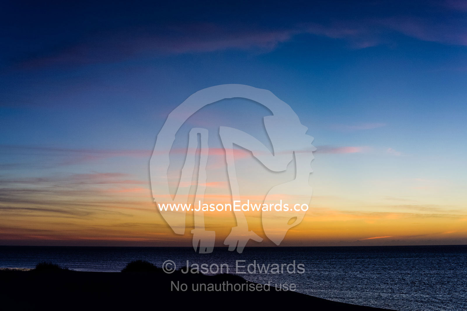 A sunset afterglow silhouettes a coastal sand dune by a tropical sea. Cape Range National Park, Exmouth, Ningaloo Reef, Western Australia, Australia.