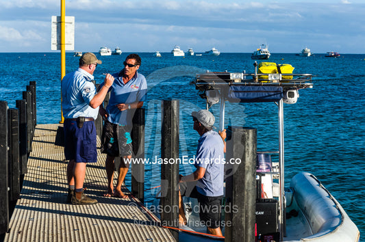 A marine police officer questions a boat captain moored at a jetty. Exmouth, Ningaloo Reef, Western Australia, Australia.