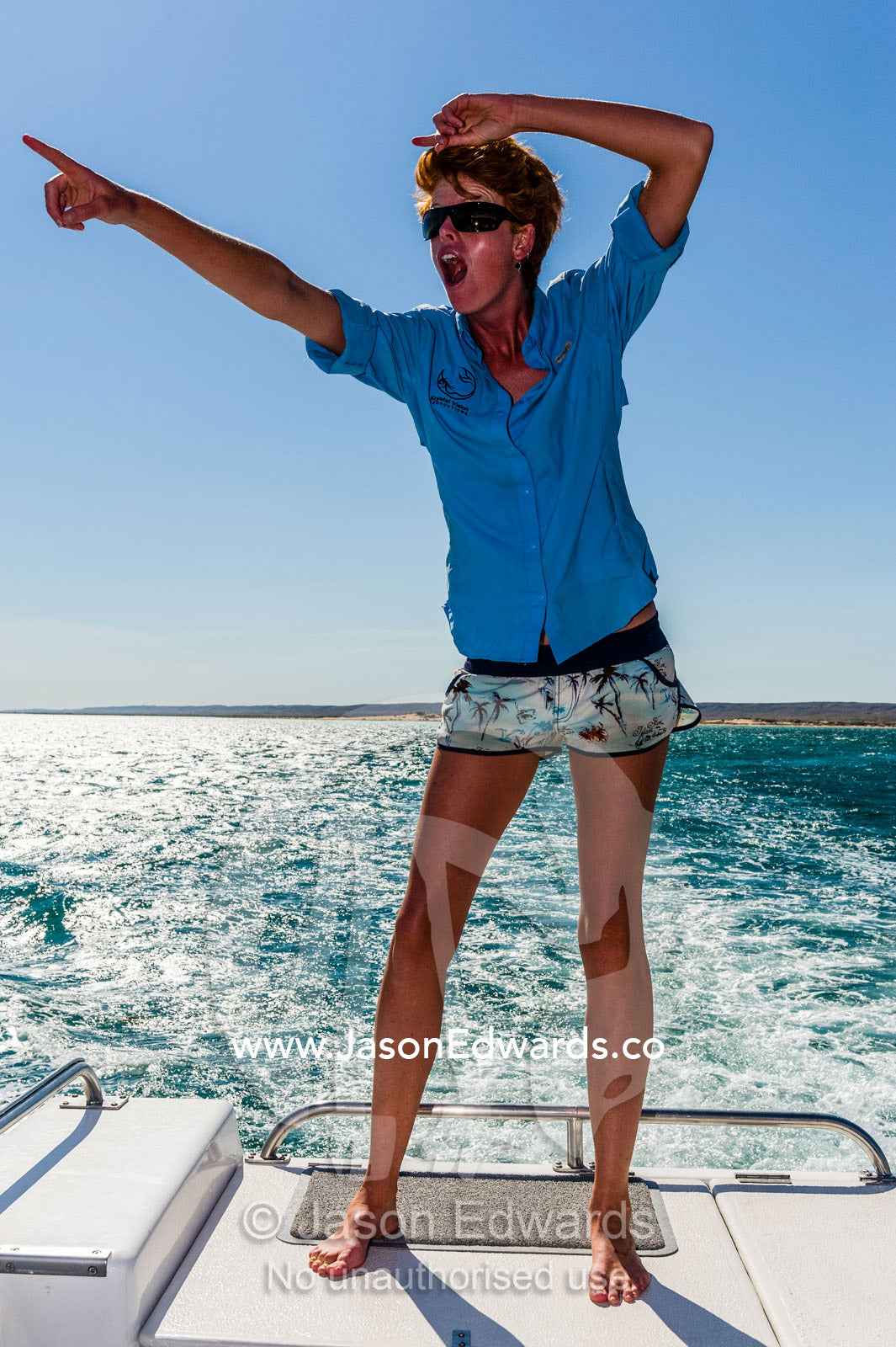 A tall lady points to the horizon on the deck of a boat off the coast. Exmouth, Ningaloo Reef, Ningaloo Marine Park, World Heritage Site, Western Australia, Australia.