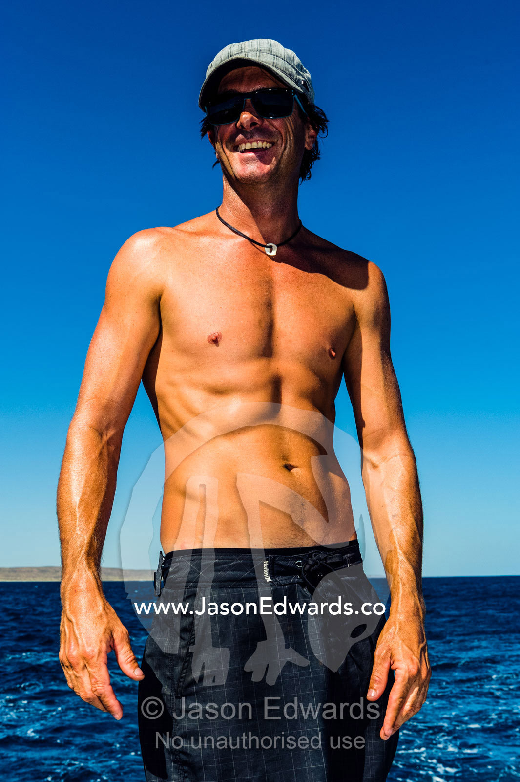 A tanned fit man standing on the deck of a boat at sea. Exmouth, Ningaloo Reef, Ningaloo Marine Park, World Heritage Site, Western Australia, Australia.