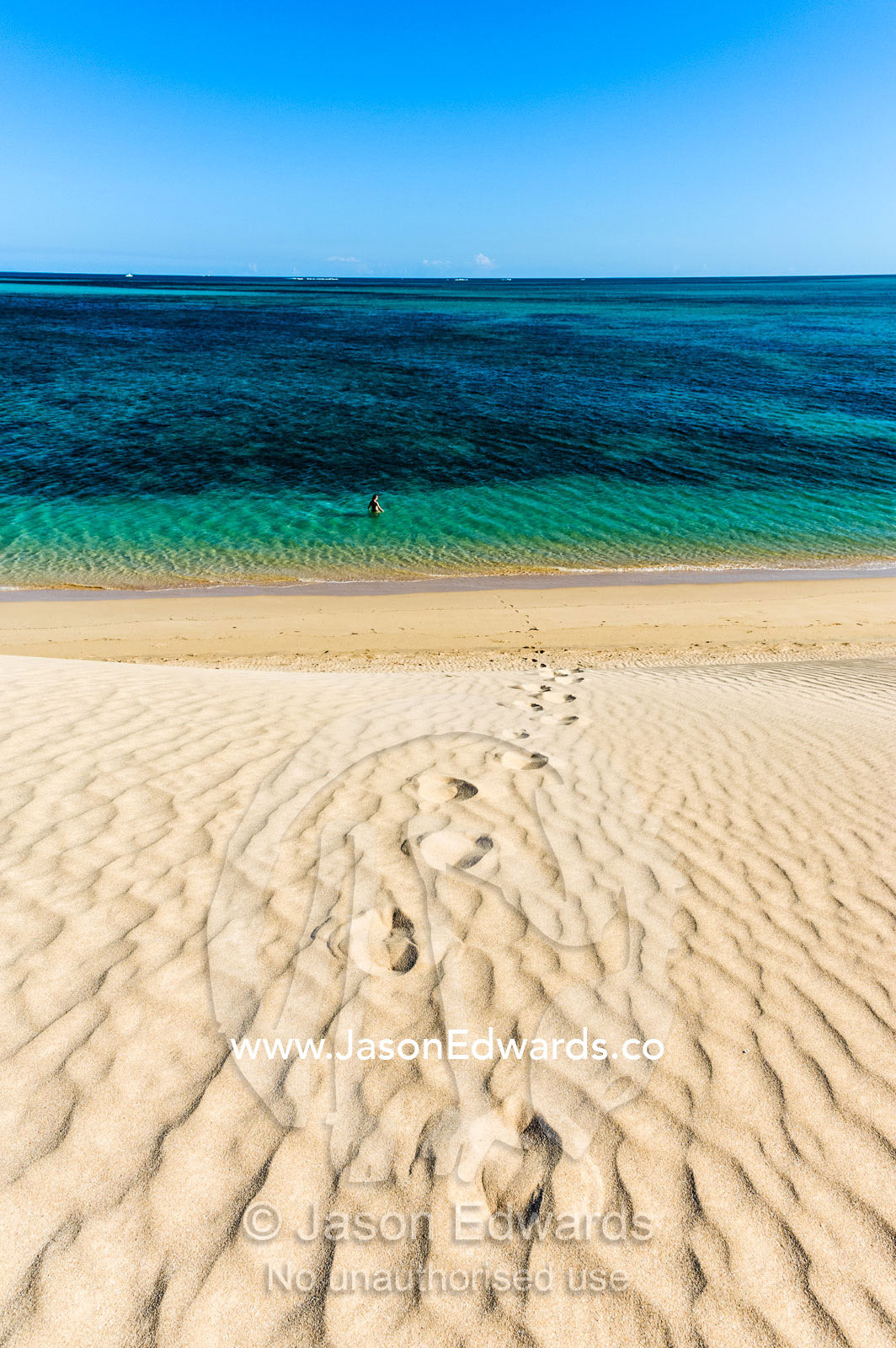 A lone swimmer hikes down a sand dune into turquoise seas to cool off. Cape Range National Park, Exmouth, Ningaloo Reef, Western Australia, Australia.