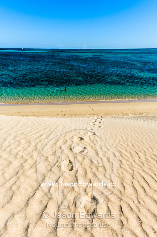A lone swimmer hikes down a sand dune into turquoise seas to cool off. Cape Range National Park, Exmouth, Ningaloo Reef, Western Australia, Australia.