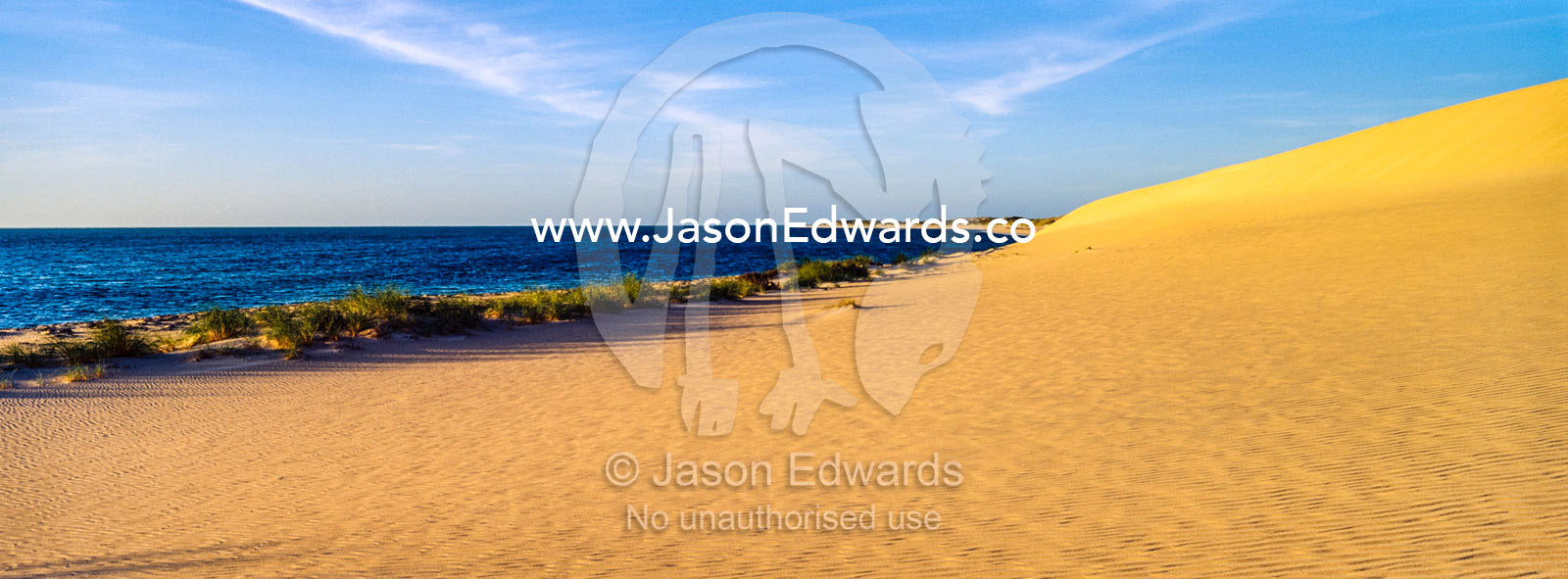 A calm sea laps the shore of a coastal desert sand dune at sunset. Cape Range National Park, Exmouth, Ningaloo Reef, Western Australia, Australia.