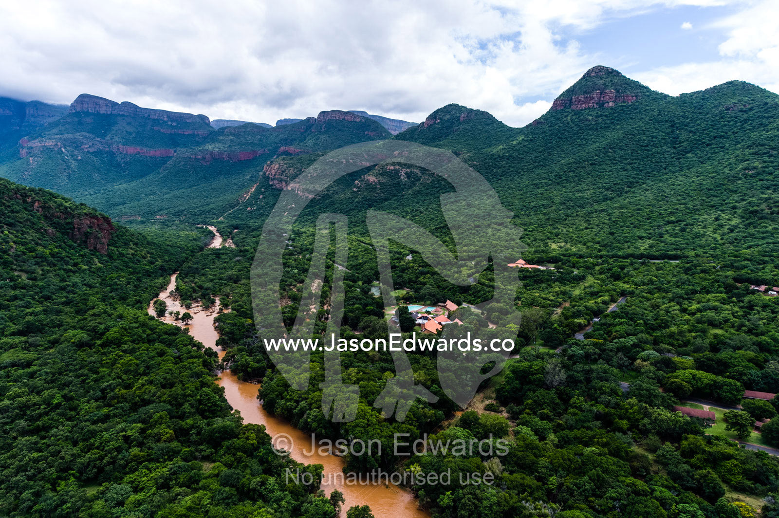 A river passes through a forested valley floor below mountain peaks. Blyde River Canyon, South Africa.