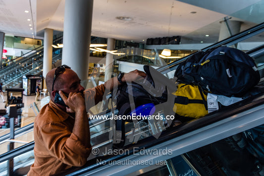 A photographers assistant moving camera equipment up an escalator. Cape Town, Western Cape, South Africa.