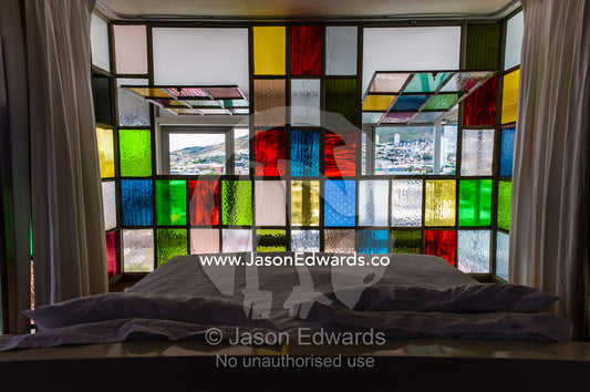 A colorful stained glass window wall surrounding an apartment bedroom. Cape Town, Western Cape, South Africa.