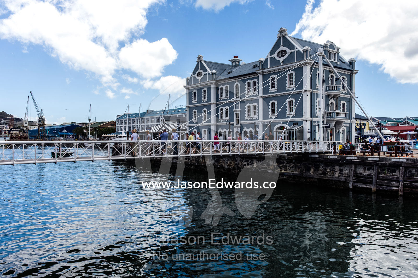 Pedestrians cross a bridge between wharves in a marina precinct. Cape Town, Victoria and Alfred Waterfront, Western Cape, South Africa.