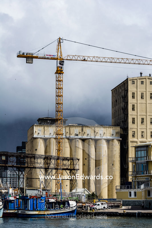 Cranes and grain silos overshadow a factory wharf and fishing boats. Cape Town, Victoria and Alfred Waterfront, Western Cape, South Africa.