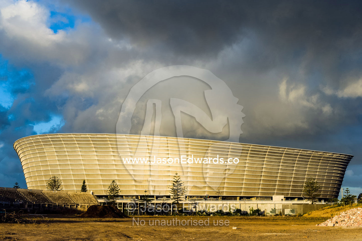 A storm turns the architecture of Cape Town Stadium golden at sunset. Cape Town Stadium, Cape Town, Western Cape, South Africa.