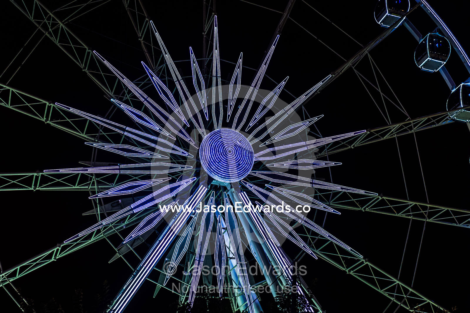 A ferris wheel illuminated by neon lights in a marina shopping district. Cape Town, Victoria and Alfred Waterfront, Western Cape, South Africa.